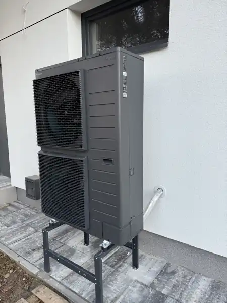 Dwuwentylatorowa jednostka zewnętrzna pompy ciepła Panasonic Aquarea na stelażu przy elewacji domu